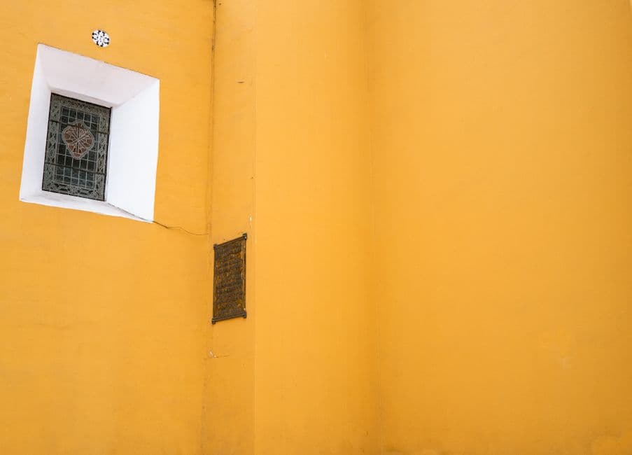 A vibrant yellow wall with a decorative window and plaque, offering bold color contrast.