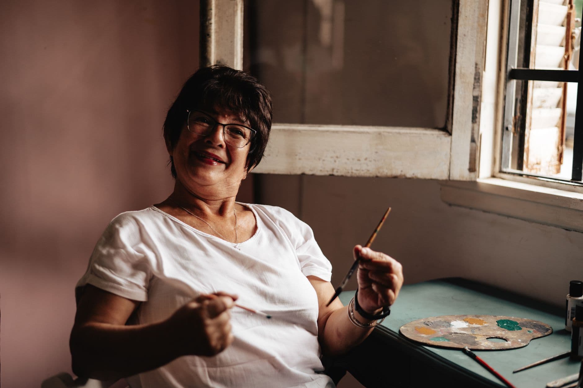 A joyful senior woman artist holding a paintbrush in her cozy Buenos Aires studio.