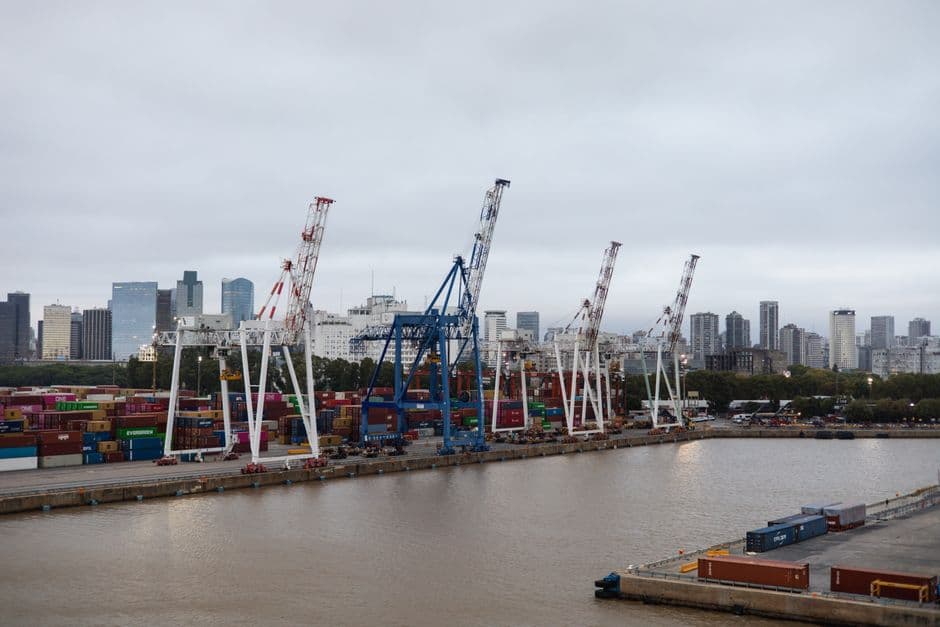 Shipping containers and cranes at a bustling port with city skyline backdrop.