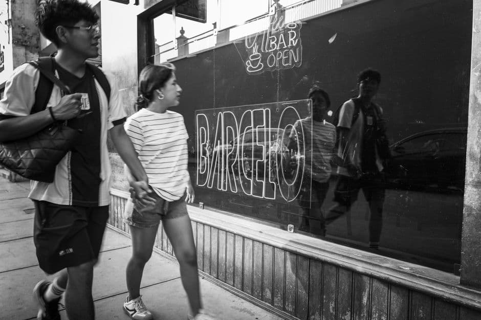 Black and white photo of a couple walking past a reflective storefront in Lima, Peru.