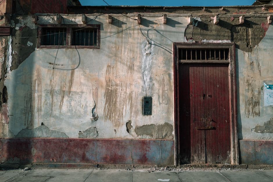 Weathered facade with red door and peeling paint in Trujillo, Peru, showing urban decay.