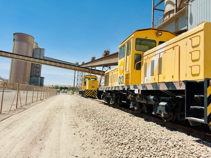 Yellow industrial trains on a railway track next to a cement plant on a clear day.