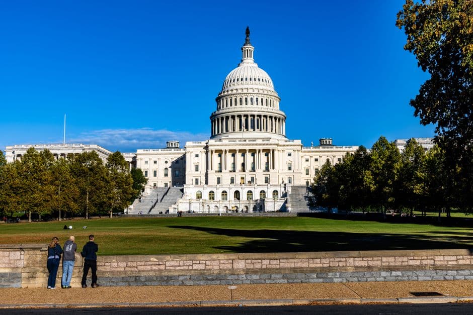 A vibrant daytime photograph of the iconic US Capitol with a clear blue sky backdrop.