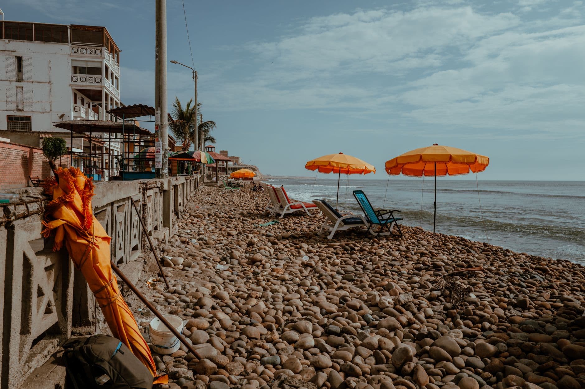 Scenic pebbled beach in Pacasmayo, Peru with vibrant umbrellas and lounge chairs.