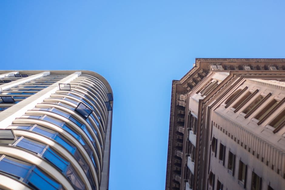 Two urban skyscrapers reach towards a clear blue sky, showcasing modern and classic architectural styles.