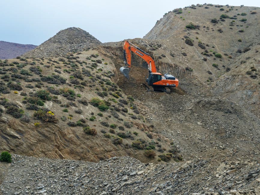 An excavator operates on a rocky hillside, illustrating industrial earthmoving in a rugged terrain.