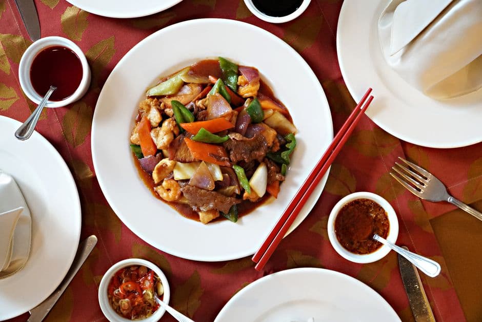 A vibrant stir-fry dish featuring vegetables and meats served with red chopsticks on a restaurant table.