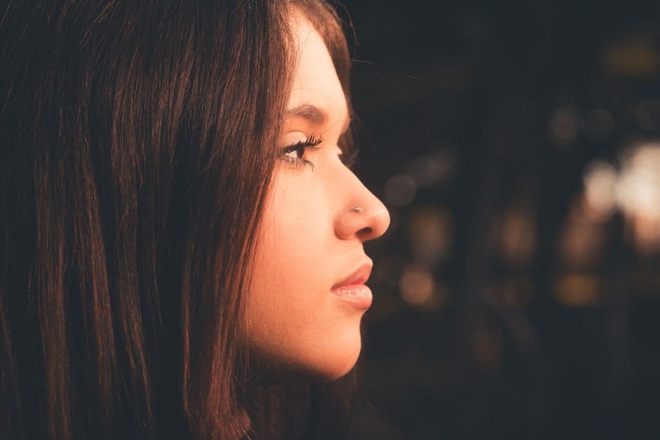 Profile portrait of a young woman with long hair and nose piercing against a blurred background.