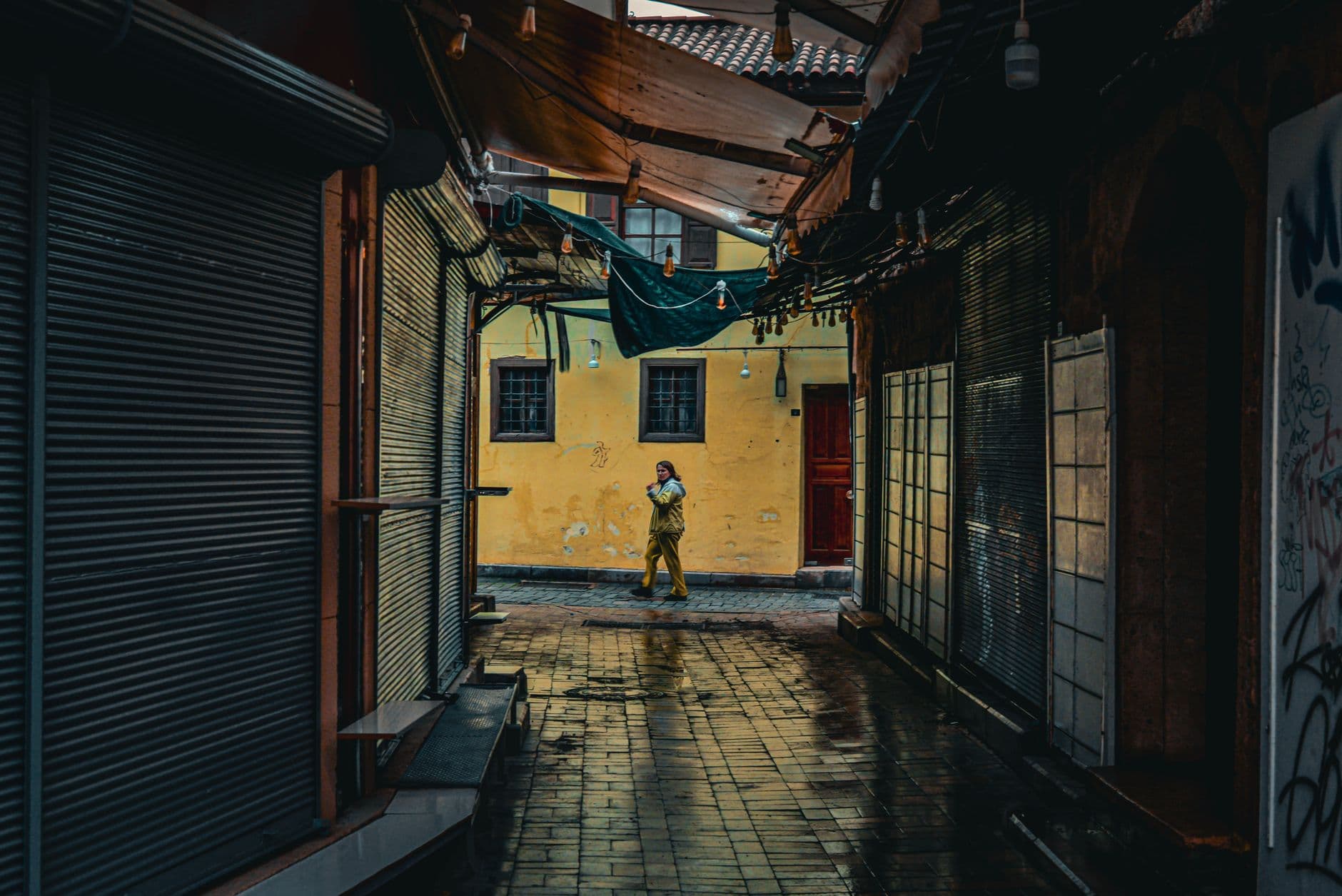 A lone person walks through a narrow, atmospheric alley in Antalya, Türkiye. Twilight casts an urban glow.