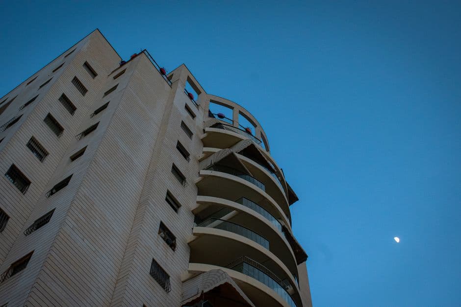 Low-angle view of a modern building with balconies against a blue evening sky featuring the moon.