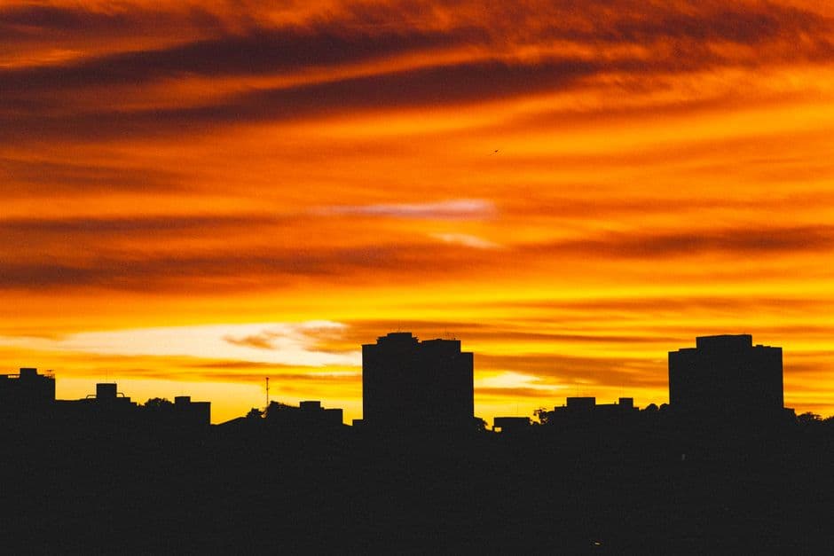 Picturesque low angle view of colorful sky with clouds illuminating silhouettes of buildings at sunset in dusk