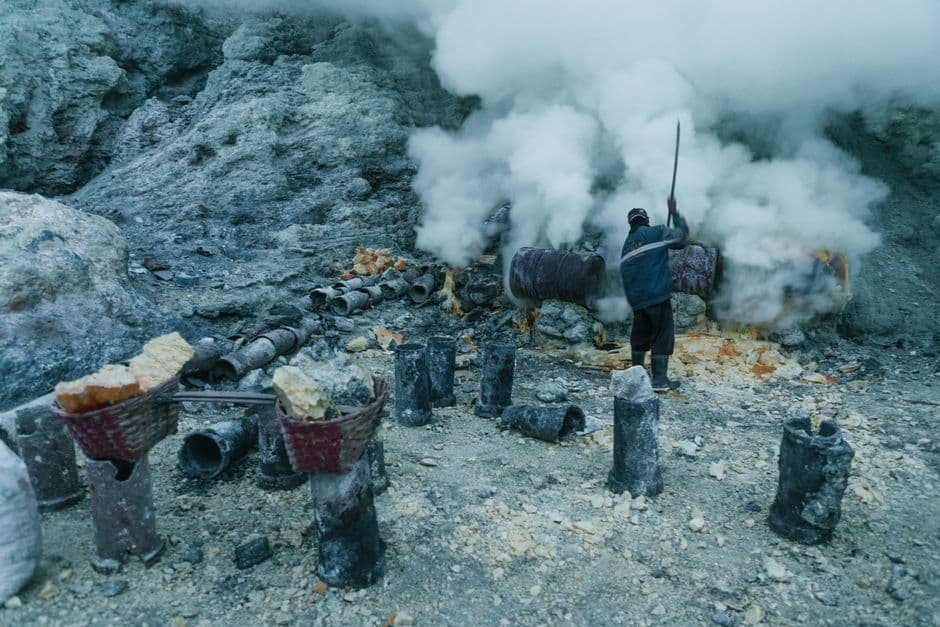 A sulfur miner working amid smoke in a rocky volcanic terrain.