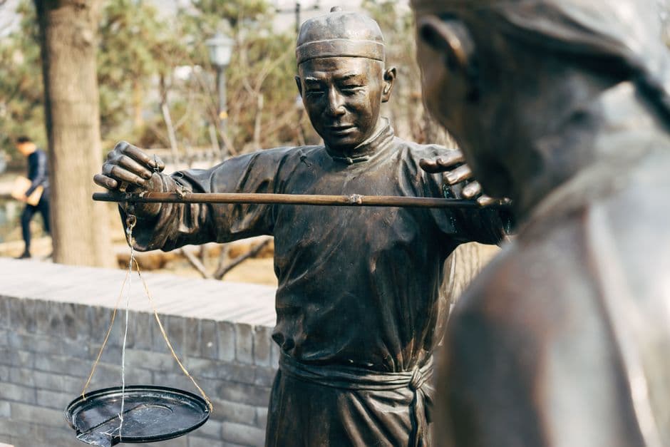 Bronze statues depicting traditional Chinese weighing scales at an outdoor market.