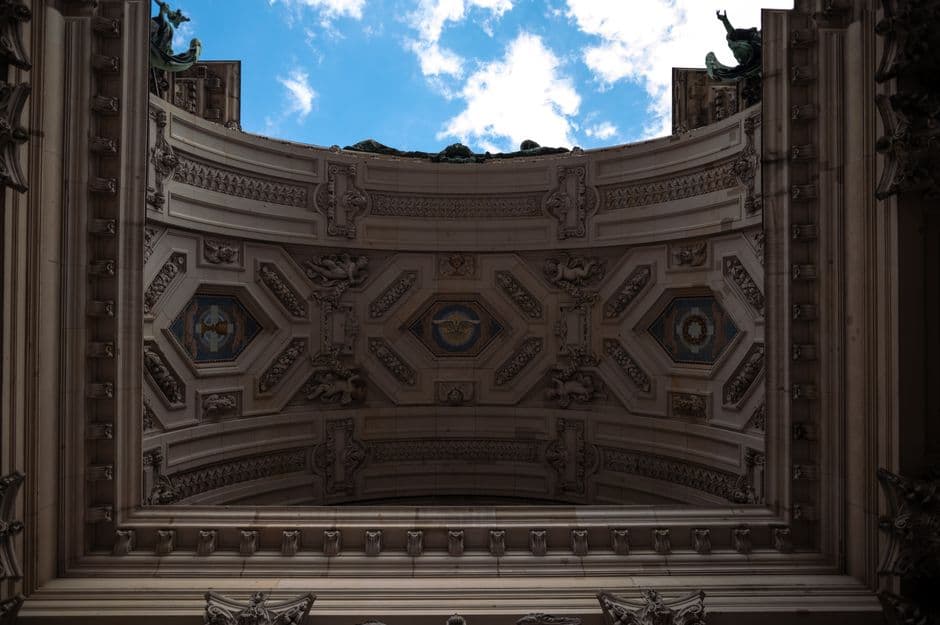 Detailed architectural ceiling with intricate designs and a glimpse of blue sky above.