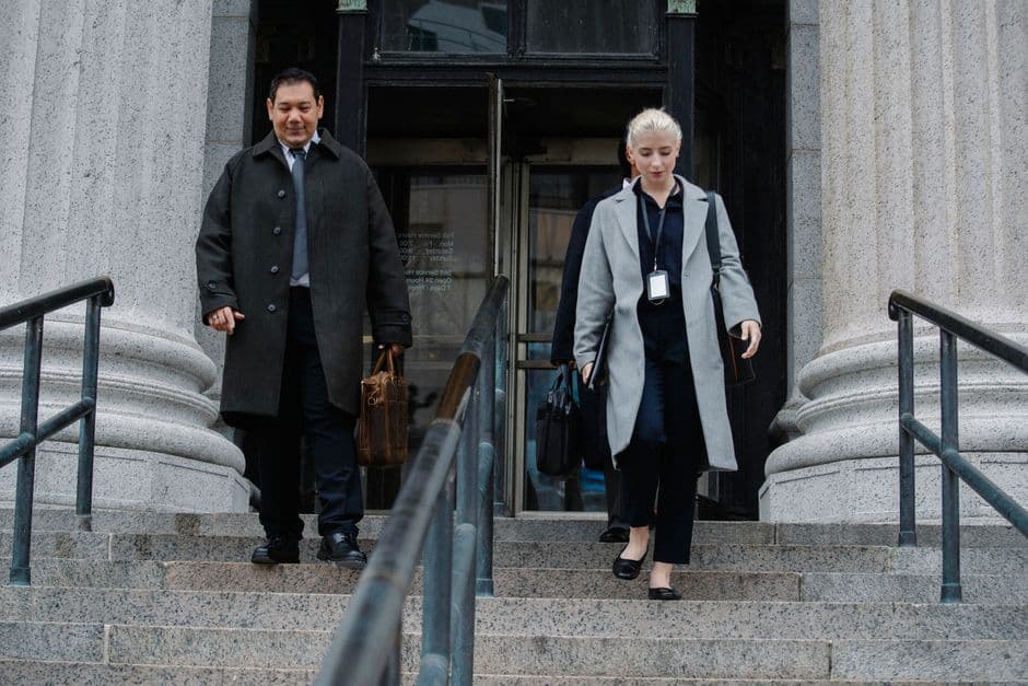 Young multiethnic colleagues in formal apparel walking on staircase of old building in town