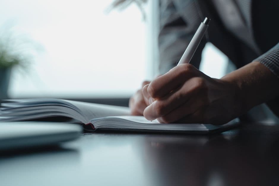 A person writing in a notebook with a pen, focusing on the hand and paper.