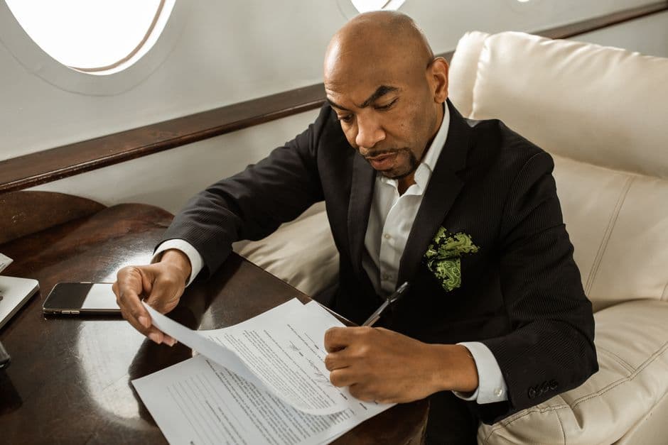 Serious businessman in black suit signing papers onboard a private jet, focusing on work.