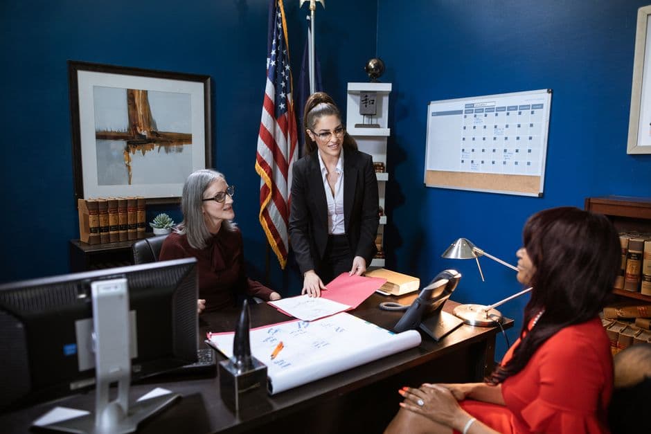 Three professional women in a business meeting discussing paperwork in a well-appointed office.