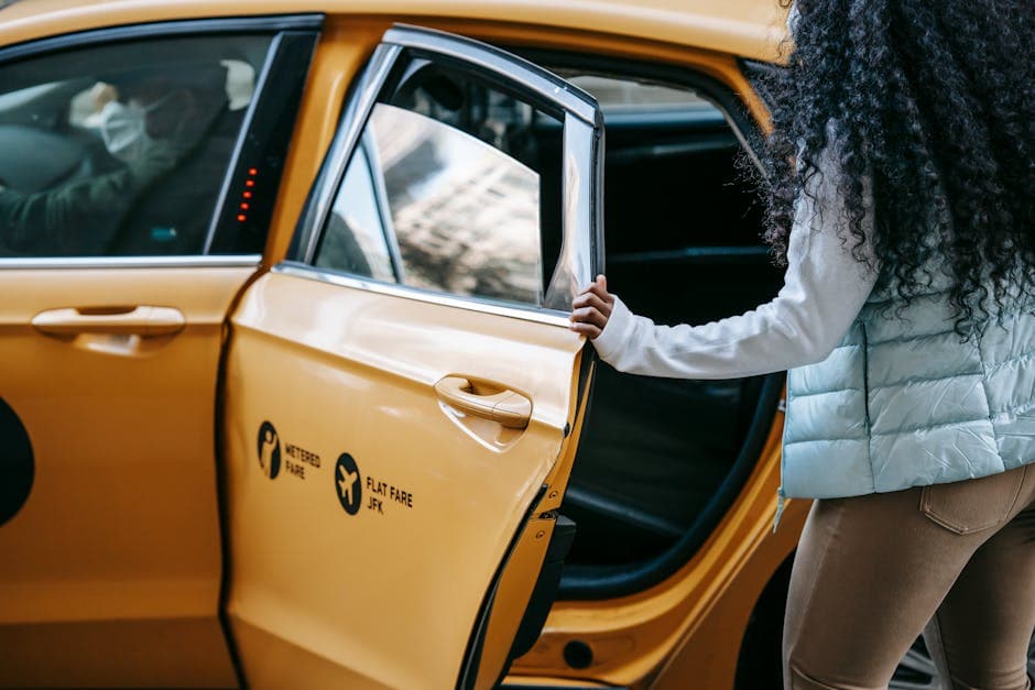 Side view of crop unrecognizable ethnic female with long Afro hair in casual outfit getting into yellow taxi on street during coronavirus