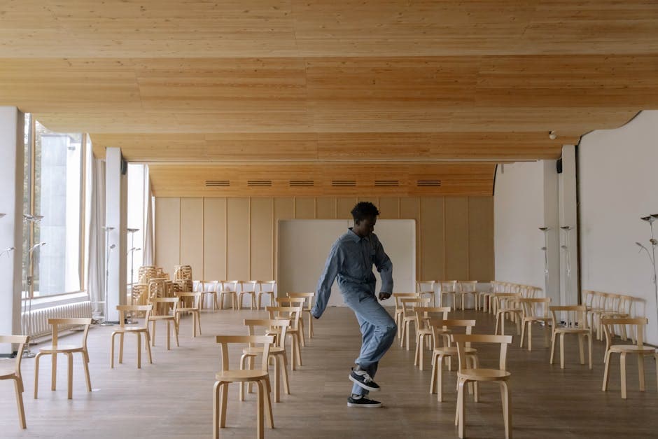 African American man dancing alone in a spacious room with wooden chairs and modern design.