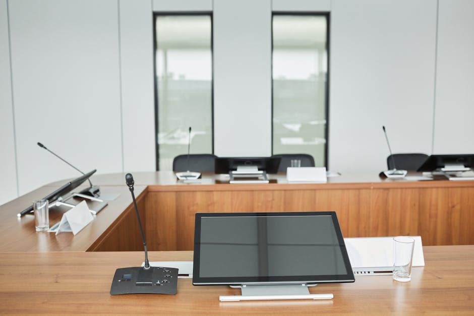 Empty conference room setup with microphones, monitors, and sleek wooden tables ready for meetings.