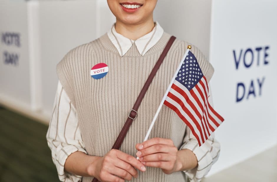 A woman proudly holds the American flag and smiles, celebrating voting day.