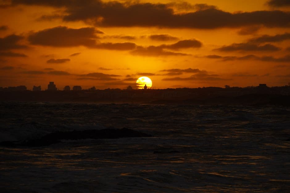 Silhouette of Punta del Este skyline with a dramatic sunset casting golden hues over the ocean.