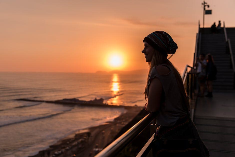 Woman enjoying a sunset by the sea in Callao, Perú, creating a serene silhouette.