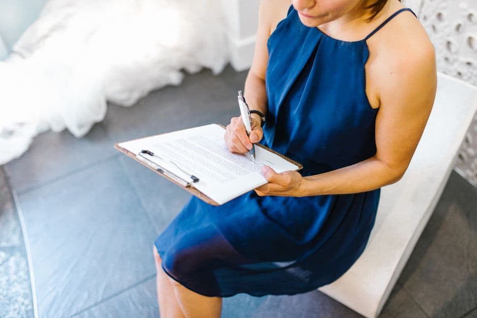 Businesswoman in blue dress writing on a clipboard indoors in a modern setting.