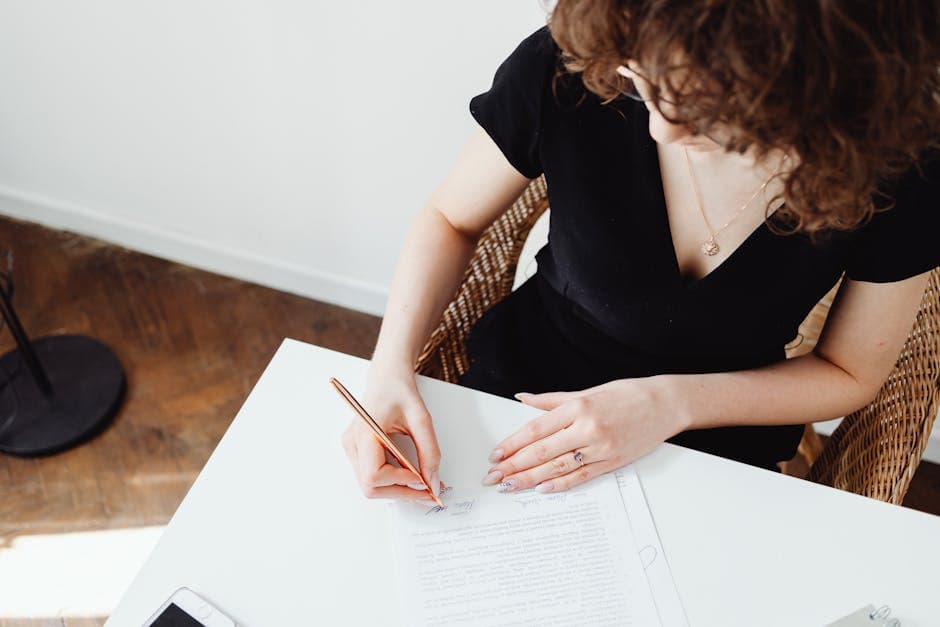 A woman writing and signing documents at a bright workspace.