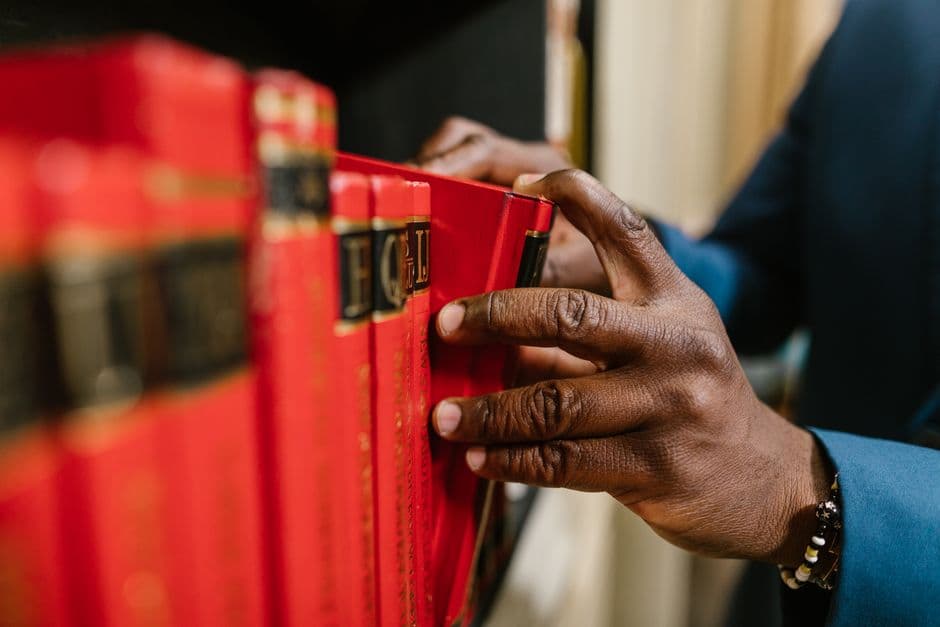 Detailed image of a hand selecting a red book from a bookshelf, focusing on texture and color contrast.