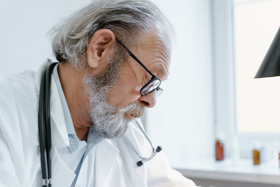Senior doctor with glasses and stethoscope focused on work in a medical office.