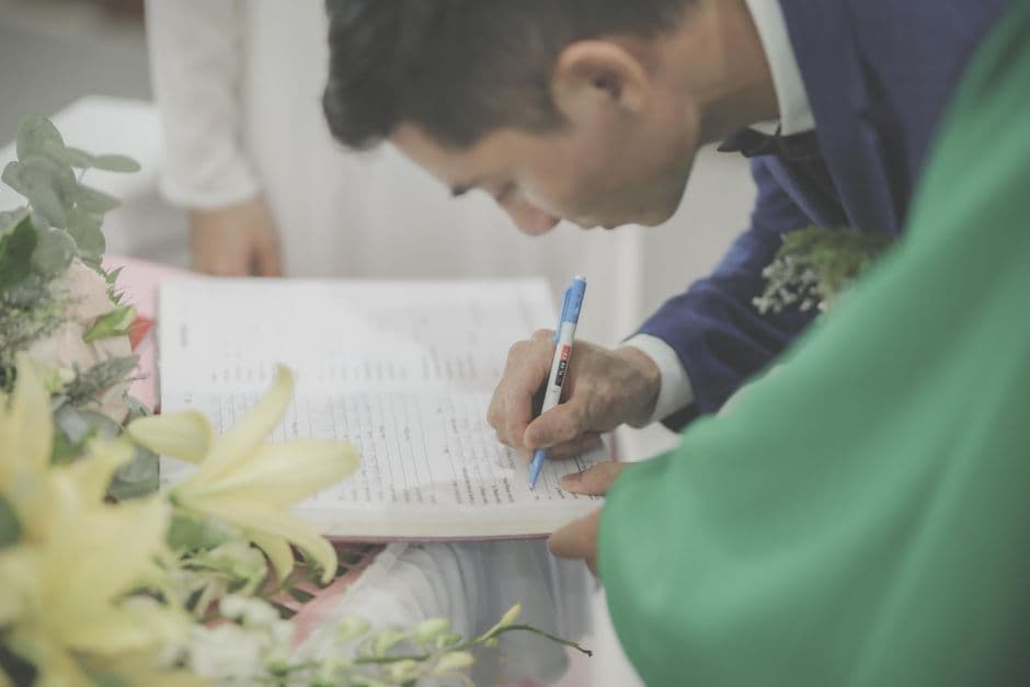 A man in formal attire signs a marriage document during a wedding celebration.