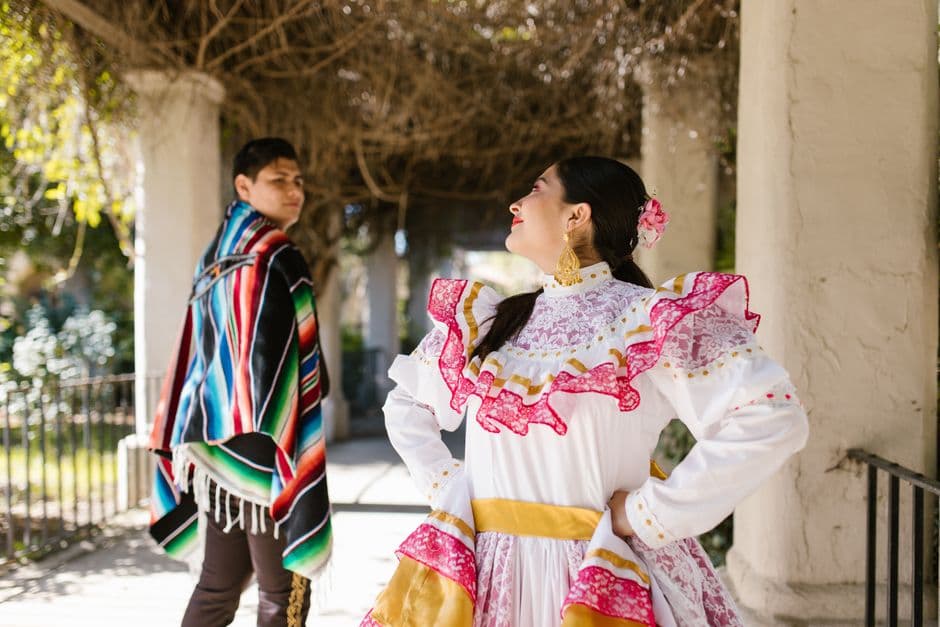 A couple in vibrant traditional clothing, celebrating Mexican culture outdoors.