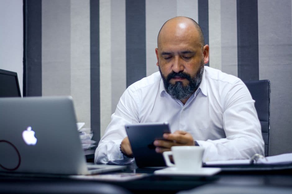 Bearded man using a tablet in a modern office environment, focusing on technology and productivity.