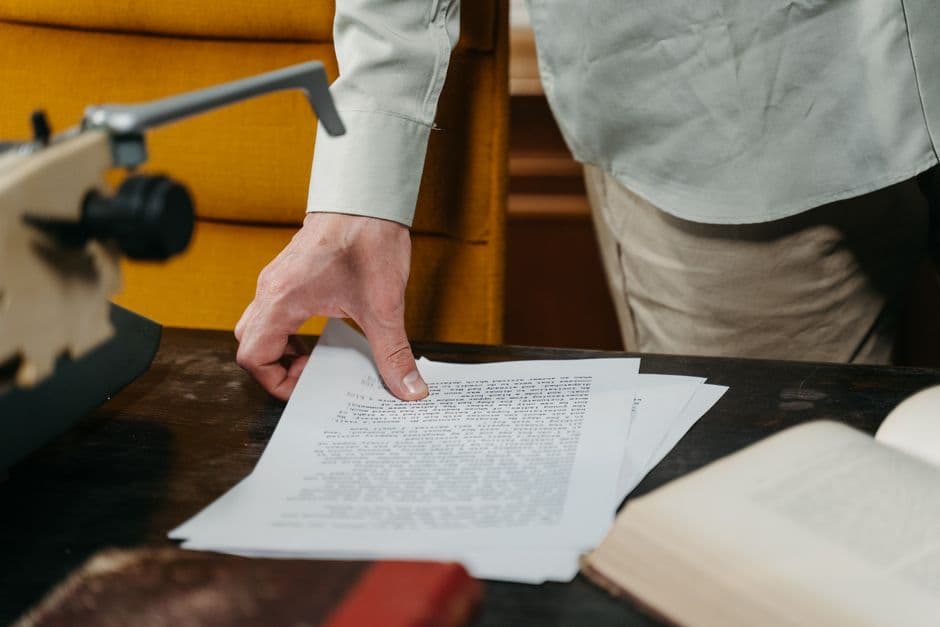 Close-up of a hand reaching for a document on a desk with a typewriter and book.