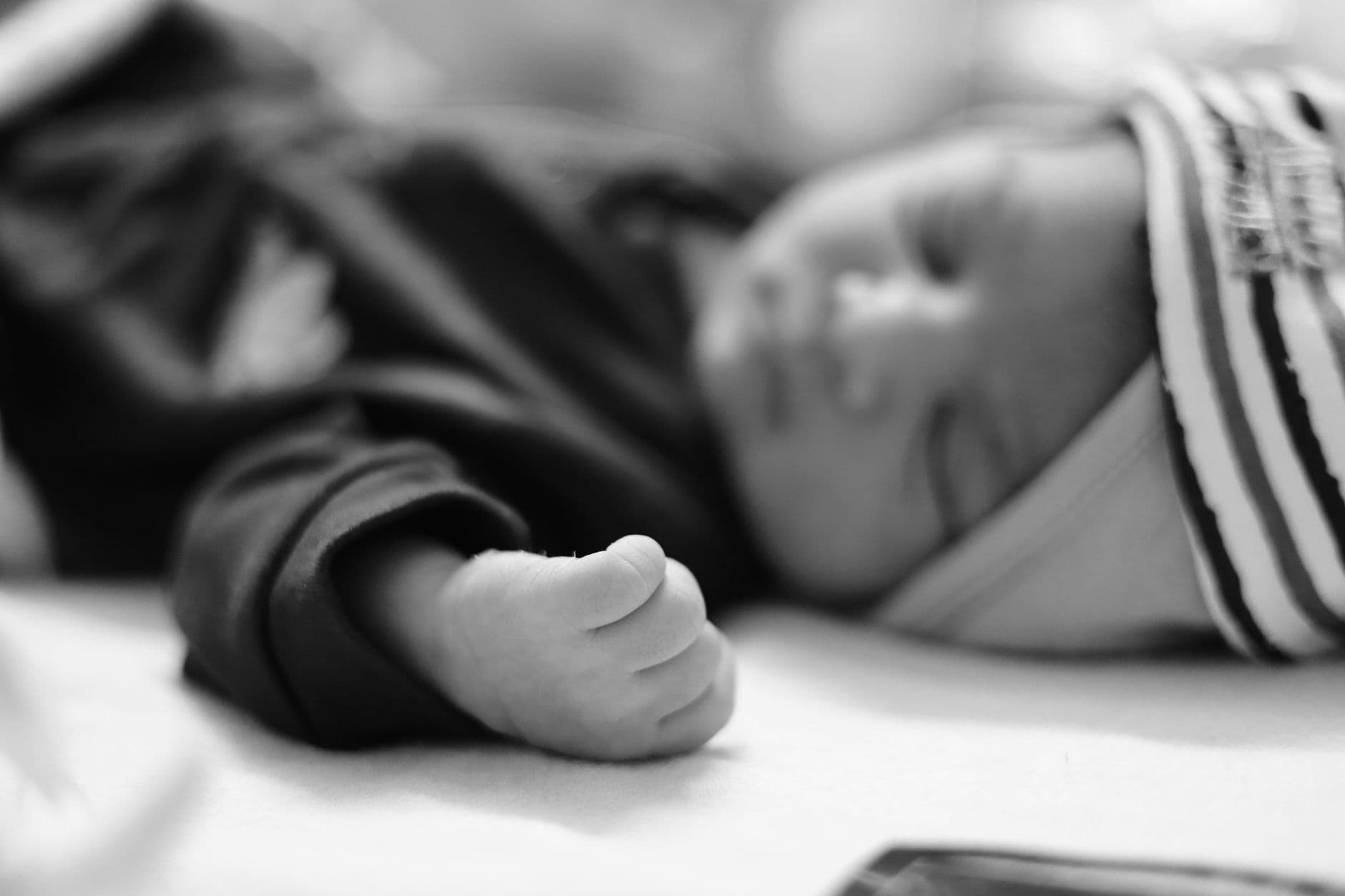 Black and white image of a newborn baby sleeping, with a close-up focus on their hand.