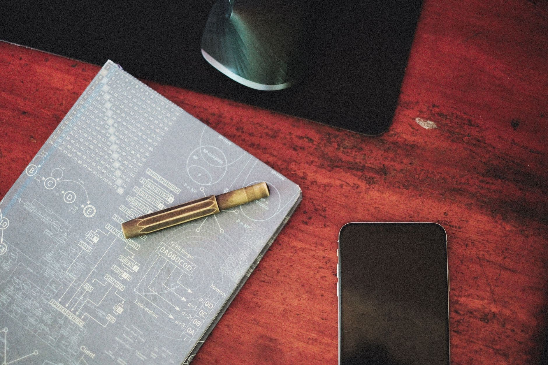 Close-up of an organized workspace featuring a cellphone, notebook, and computer mouse on a wooden desk.
