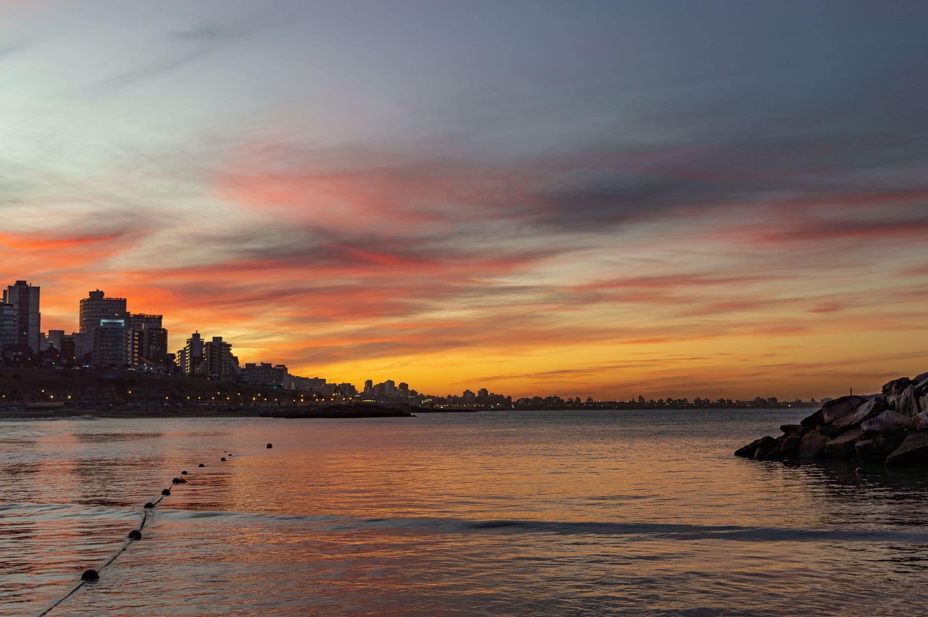 A beautiful sunset over a city's waterfront with dramatic skies and tranquil sea.