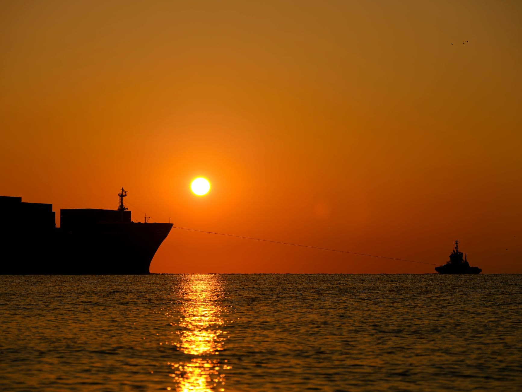 A dramatic sunset over the ocean with silhouetted ships and vivid water reflections.