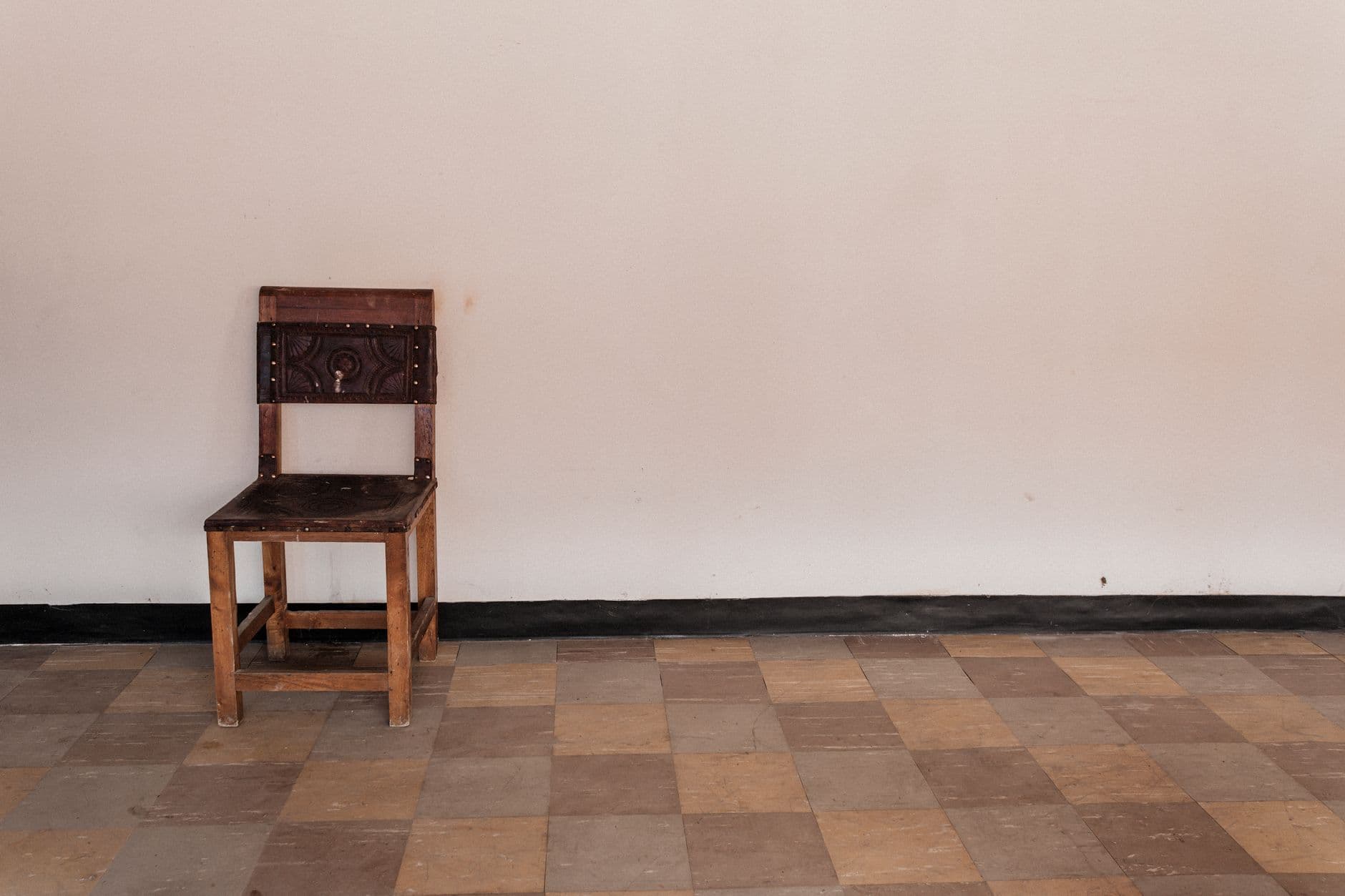 A single rustic wooden chair against a neutral wall in a minimalist room with tiled flooring.