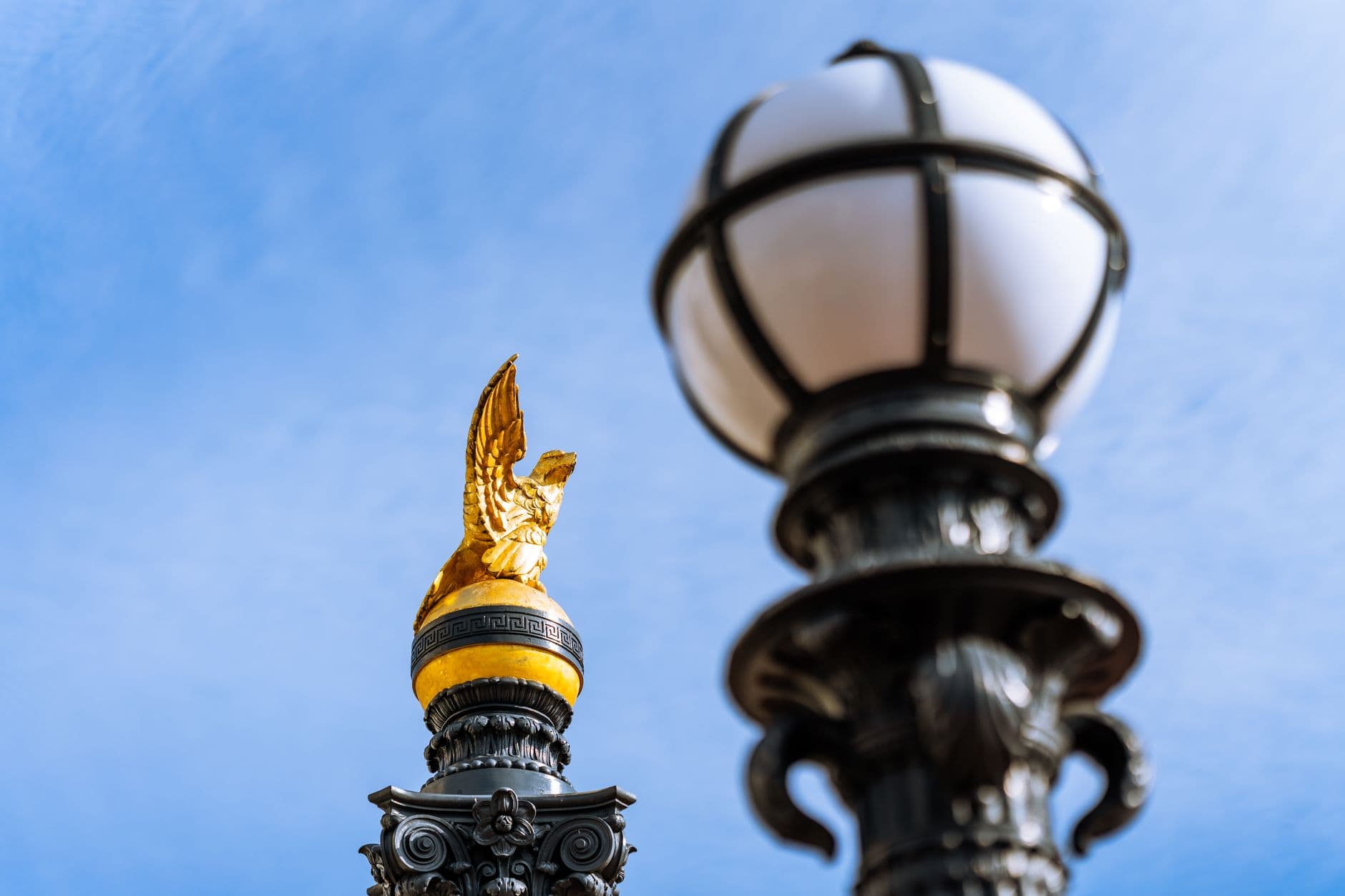 Close-up of a golden eagle sculpture and ornate street lamp against a blue sky.