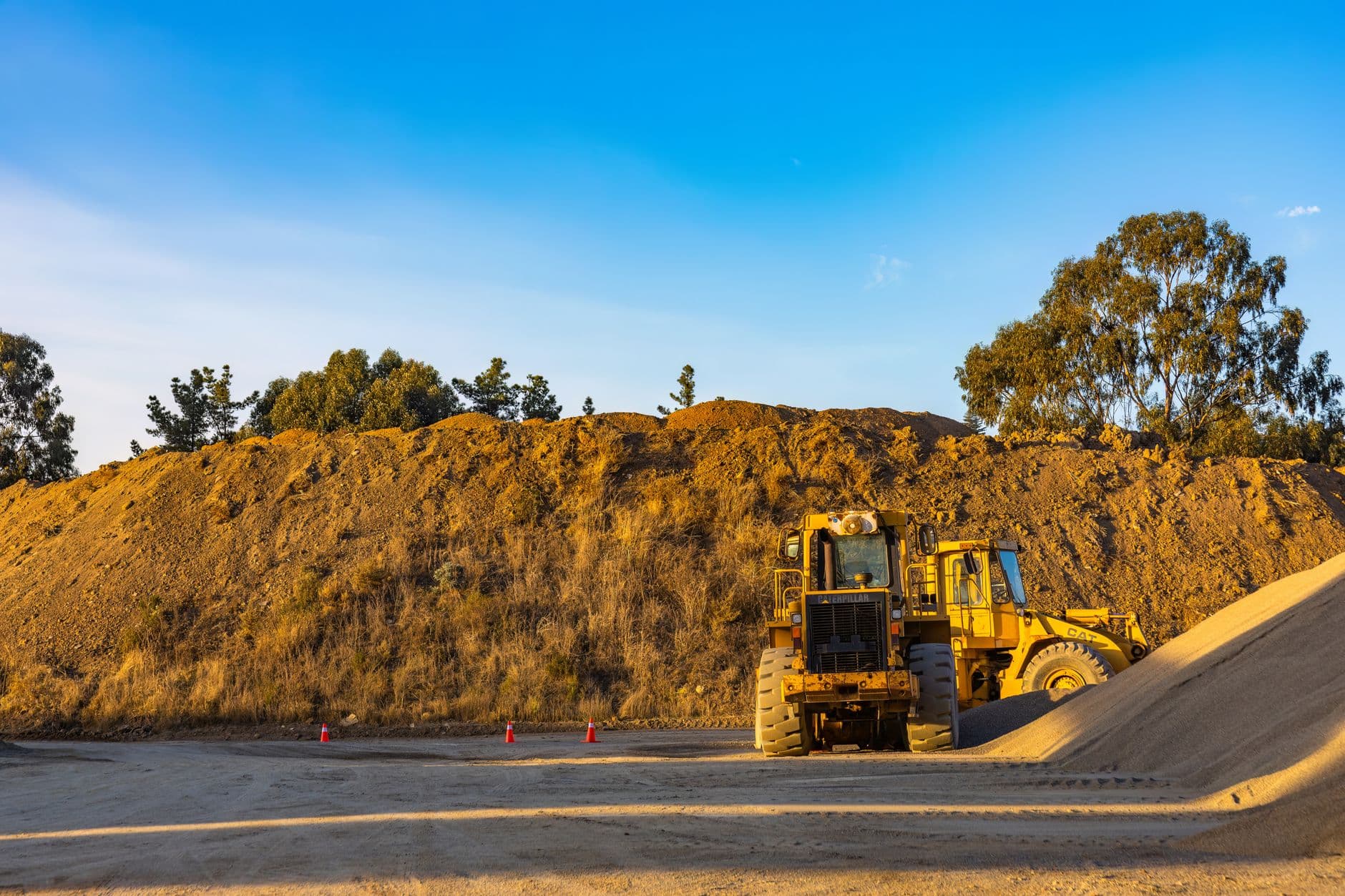 Yellow construction machinery working on a dirt pile at a rural site with a clear blue sky backdrop.