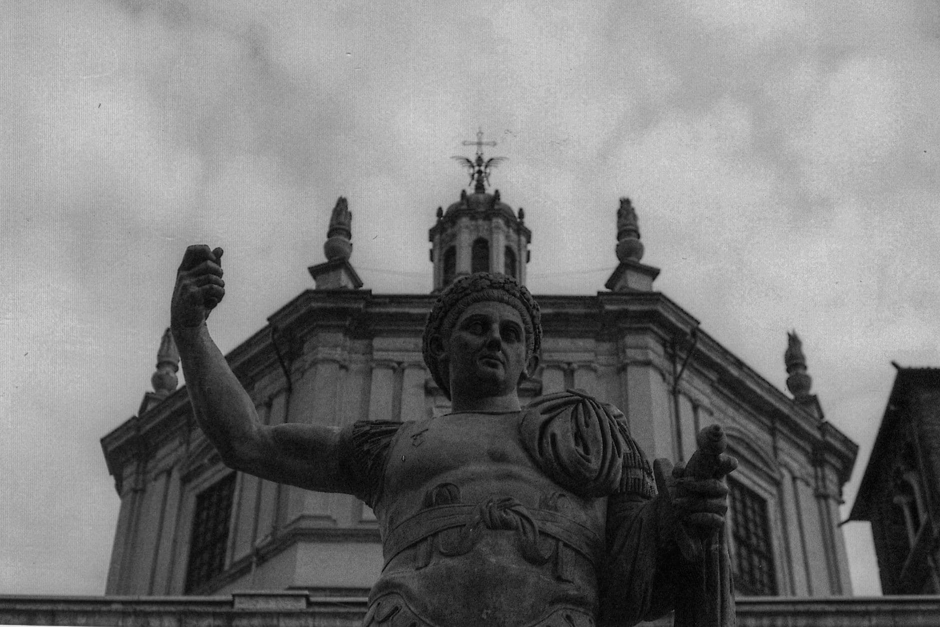 Low angle view of a historic marble statue with classical architecture in the background, set in an urban area.
