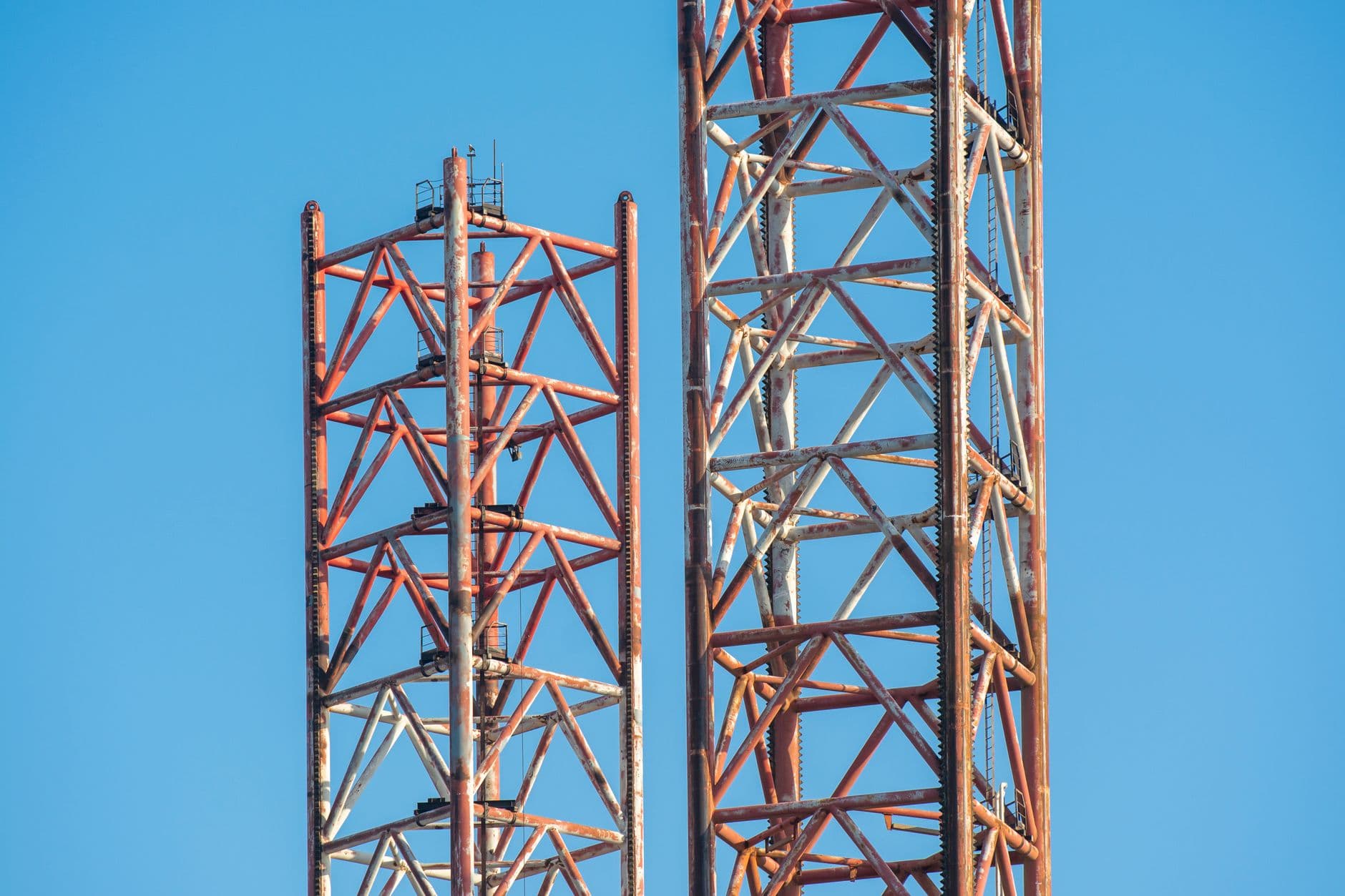 Close-up view of rusty crane towers under clear blue sky, illustrating construction industry details.