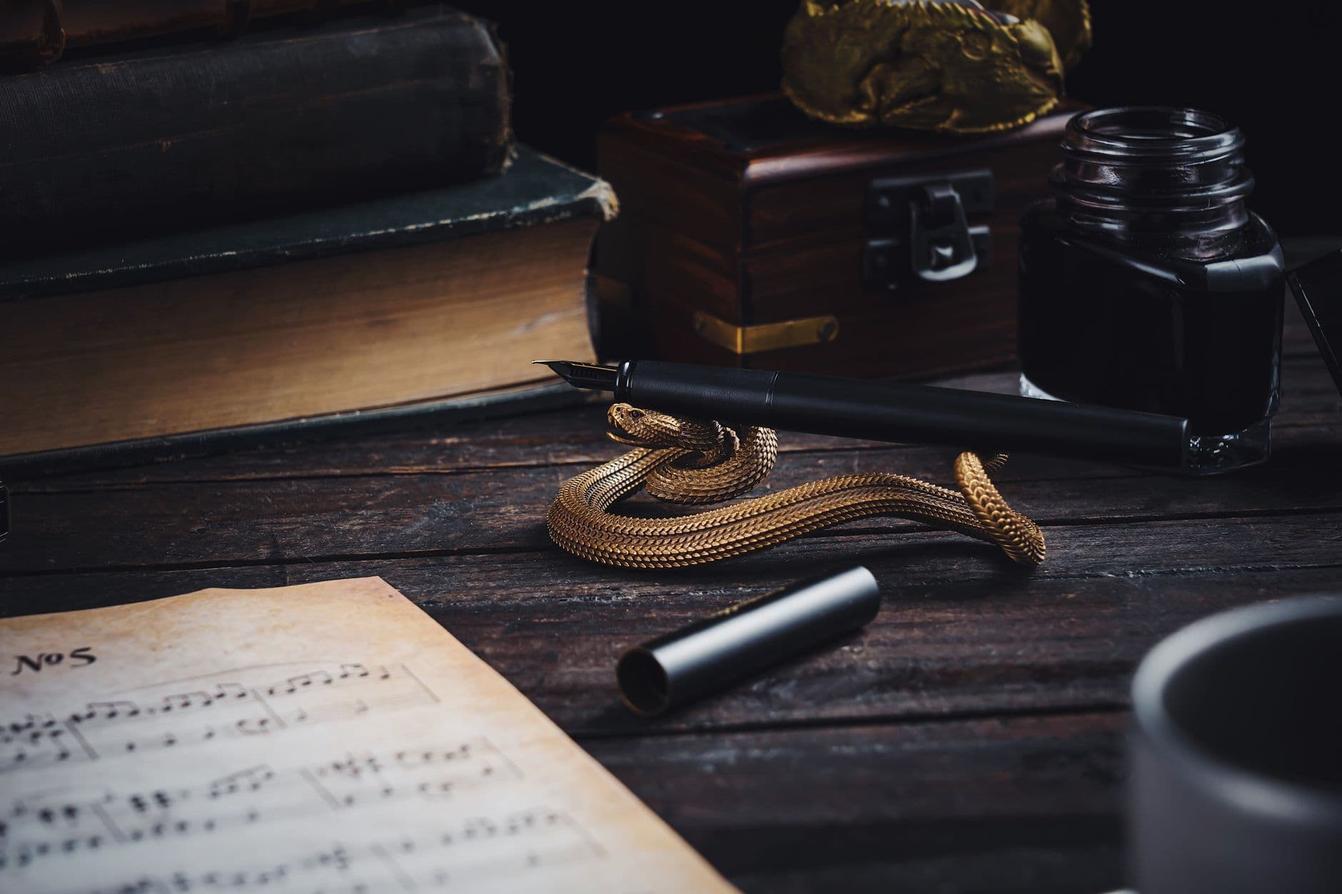 A vintage desk setup with books, quill, inkwell, and a musical sheet on a wooden surface.