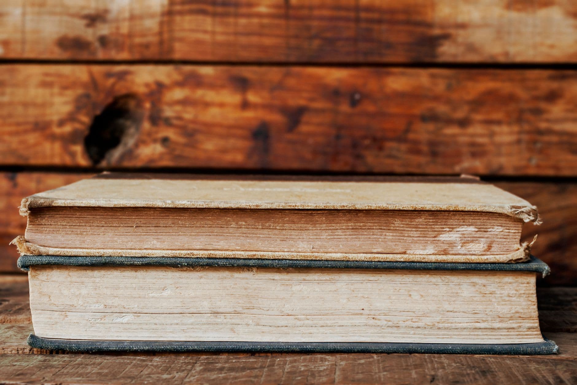 Close-up of two vintage books stacked against a rustic wooden backdrop, highlighting texture and age.