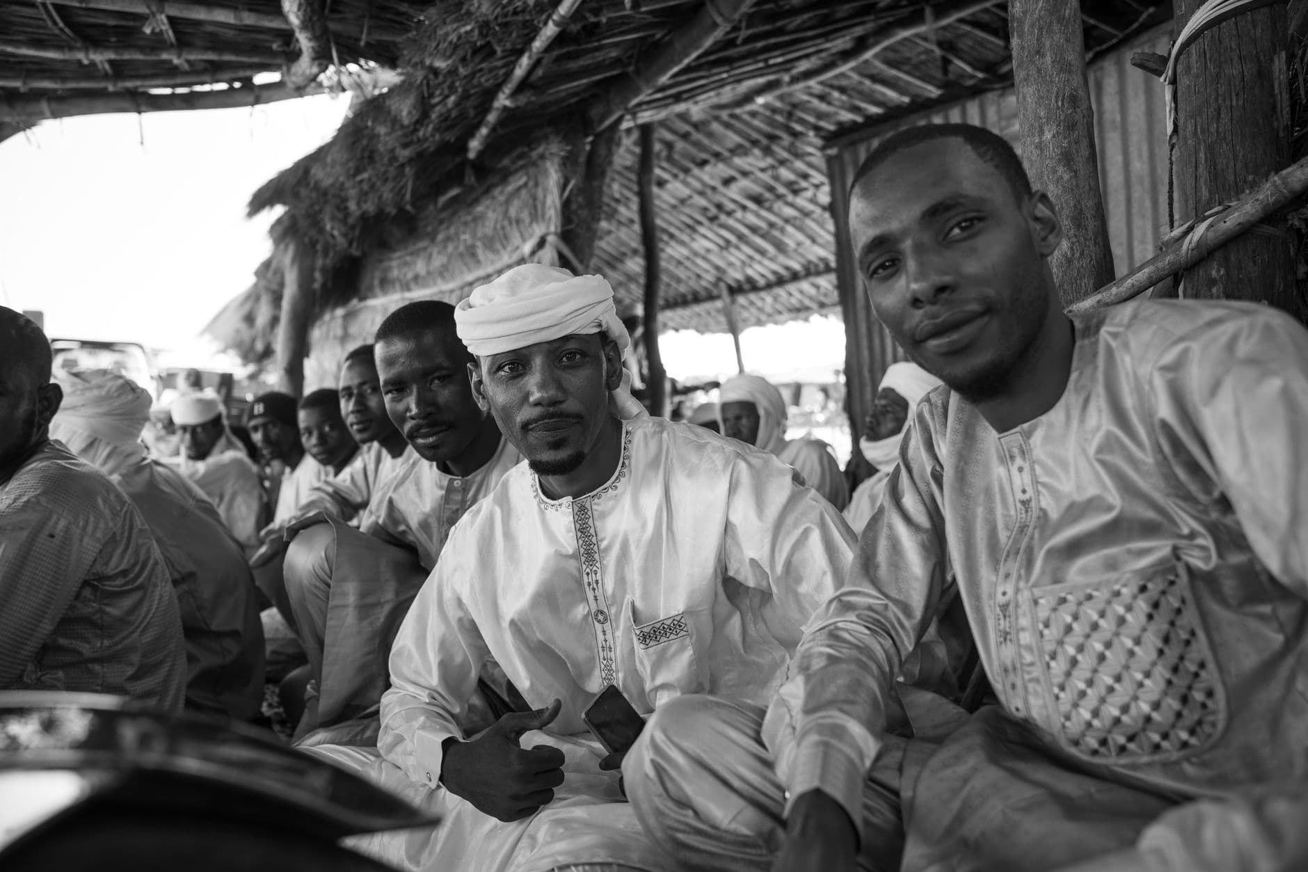 Group of men in traditional attire sitting together, captured in black and white.
