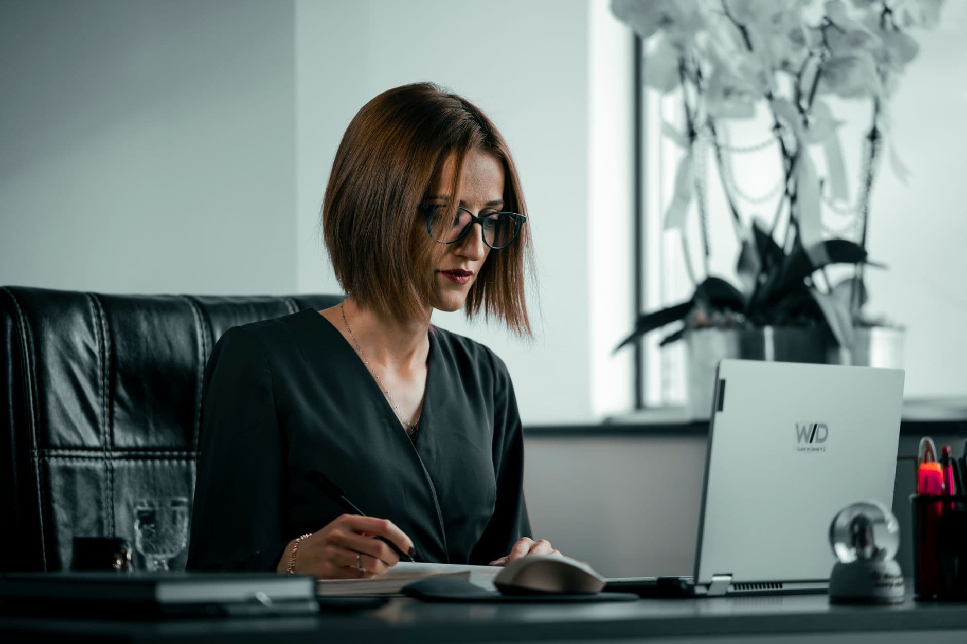 Businesswoman in an office setting, focused on work using a laptop. Elegant and professional atmosphere.
