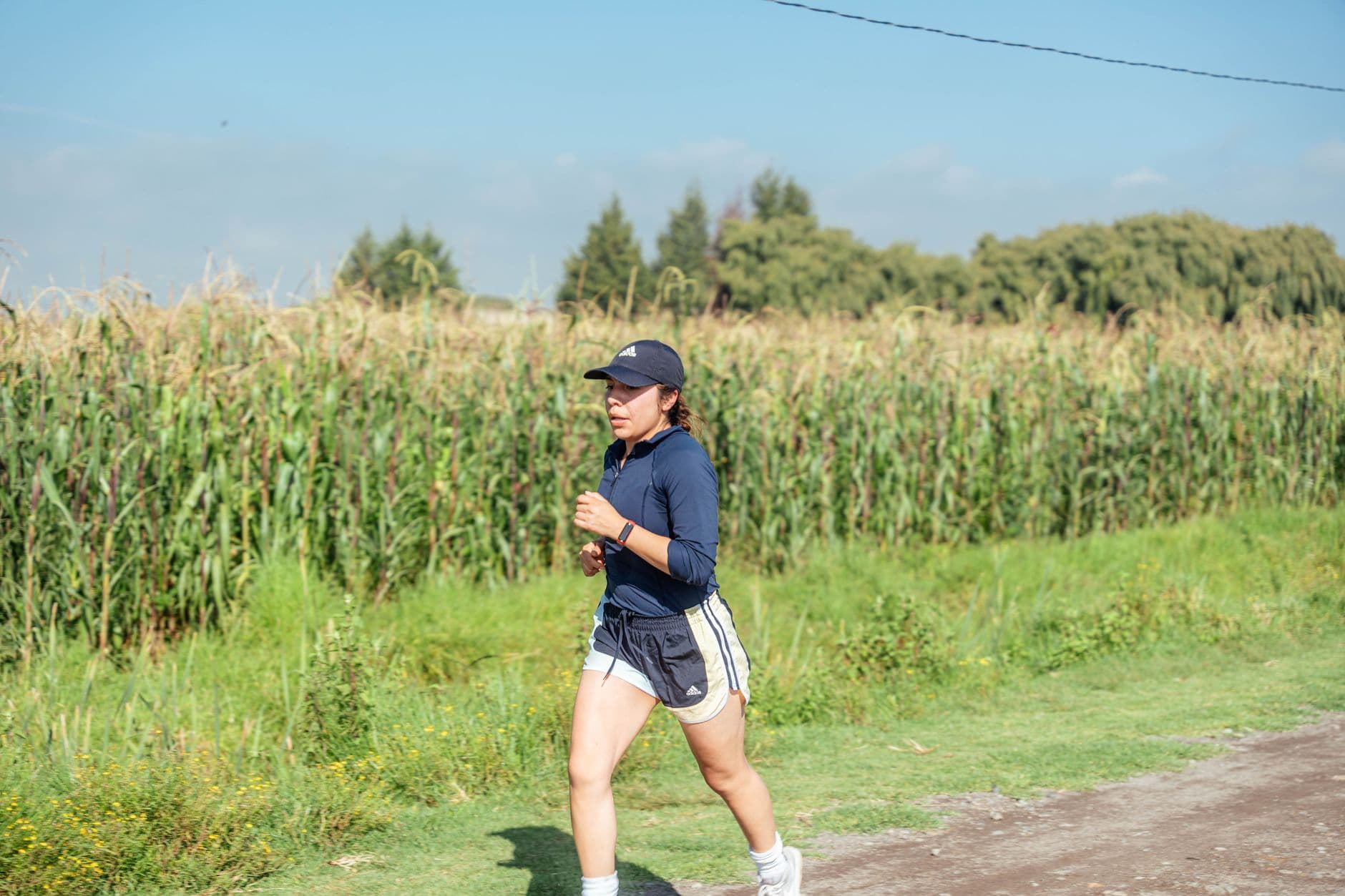 Woman jogging along a rural path next to a cornfield, enjoying fitness in nature.